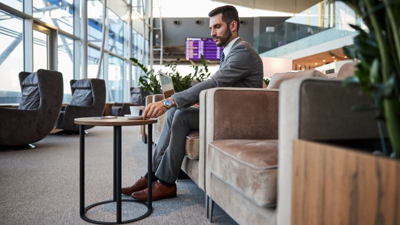imagem exibe homem sentado tomando café em sala vip de aeroporto.
